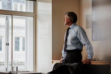 Geschäftsmann im Büro schaut nachdenklich aus dem Fenster - CUF44009