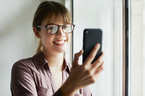 Frau schaut lächelnd auf ihr Smartphone - CUF44036
