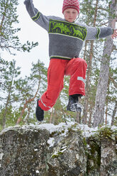 Young boy jumping from rock ledge, in rural landscape, low angle view - CUF44060