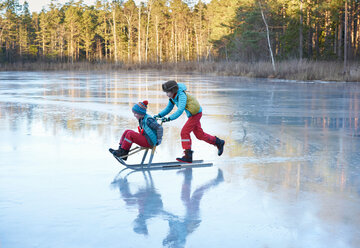 Junge schiebt seinen Bruder auf einem Schlitten über einen zugefrorenen See - CUF44112