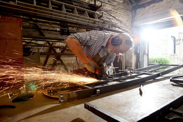 Blacksmith grinding metal on workbench in blacksmiths shop - CUF44129