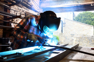 Blacksmith welding metal on workbench in blacksmiths shop - CUF44130