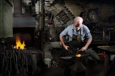 Blacksmith hammering red hot metal in blacksmiths shop - CUF44132