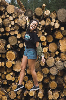 Glückliche junge Frau balanciert auf einem Holzstapel - KKAF02382