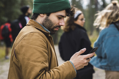 Mann überprüft Handy im Freien mit Freunden im Hintergrund, lizenzfreies Stockfoto