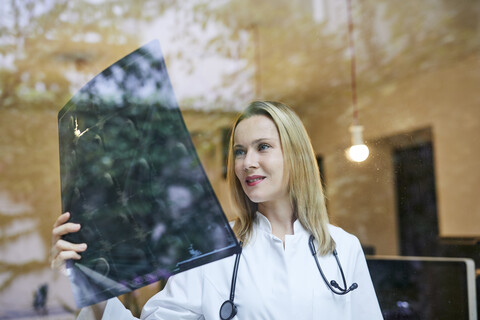 Eine Ärztin betrachtet ein Röntgenbild hinter einer Fensterscheibe, lizenzfreies Stockfoto