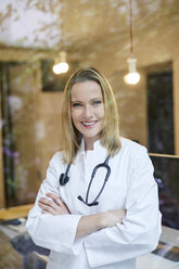 Portrait of smiling female doctor with stethoscope behind windowpane - PNEF00984