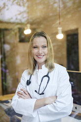 Portrait of smiling female doctor with stethoscope behind windowpane - PNEF00985