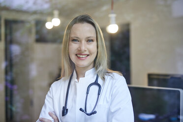 Portrait of smiling female doctor with stethoscope behind windowpane - PNEF00986