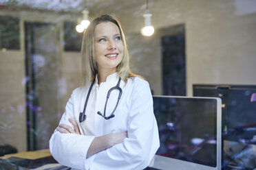 Smiling female doctor with stethoscope behind windowpane - PNEF00987