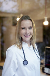Portrait of smiling female doctor with stethoscope behind windowpane - PNEF00989