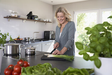 Smiling woman cutting spring onions in kitchen - PDF01723