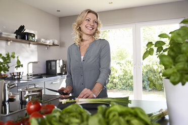 Smiling woman cutting spring onions in kitchen - PDF01726