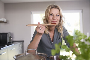 Lächelnde Frau, die in der Küche kocht und Tomatensoße probiert - PDF01735