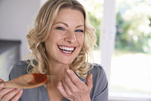 Porträt einer glücklichen Frau, die Tomatensauce vom Kochlöffel kostet - PDF01736