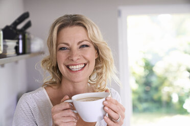 Porträt einer lächelnden Frau, die in der Küche Kaffee trinkt - PDF01738