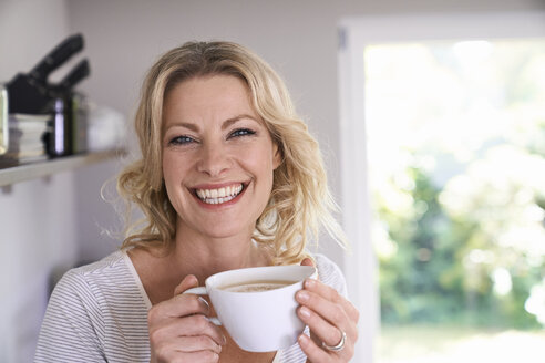 Portrait of smiling woman drinking coffee in kitchen - PDF01738