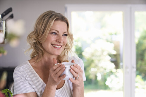 Porträt einer lächelnden Frau, die in der Küche Kaffee trinkt - PDF01739