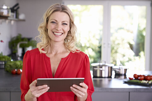 Portrait of smiling woman holding tablet in kitchen - PDF01749