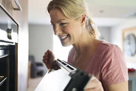Lächelnde Frau beim Kochen in der Küche mit Blick in den Ofen, lizenzfreies Stockfoto