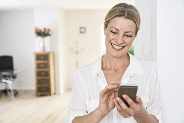 Lächelnde Frau, die zu Hause ein Mobiltelefon benutzt - PDF01763