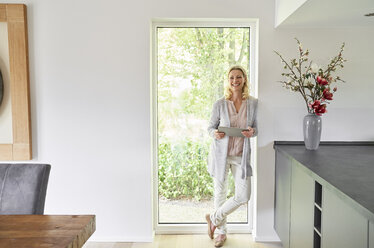 Porträt einer glücklichen Frau, die zu Hause an der französischen Tür steht und ein Tablet benutzt - PDF01775