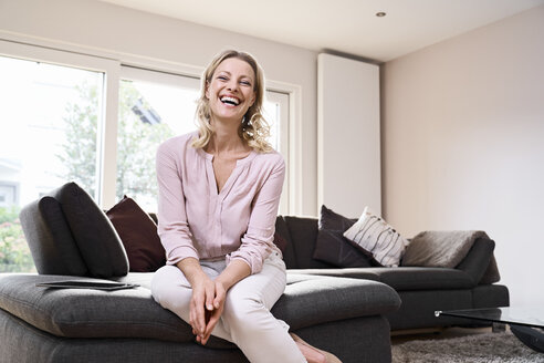 Portrait of laughing woman sitting on couch at home - PDF01778