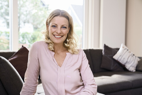 Porträt einer lächelnden Frau, die zu Hause auf der Couch sitzt, lizenzfreies Stockfoto