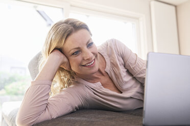 Smiling woman lying on couch using tablet at home - PDF01784