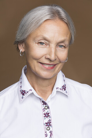 Porträt einer lächelnden älteren Frau mit grauem Haar und bestickter Bluse, lizenzfreies Stockfoto