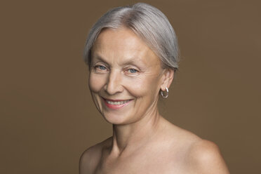 Portrait of naked senior woman with grey hair in front of brown background - VGF00008