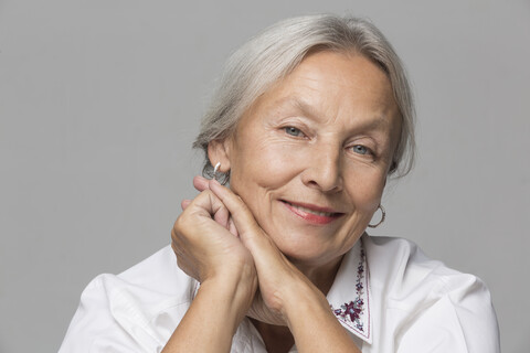 Porträt einer entspannten älteren Frau mit grauem Haar vor einem grauen Hintergrund, lizenzfreies Stockfoto