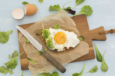 Fried egg on slice of brown bread coated with paprika cream on baking paper - JUNF01367