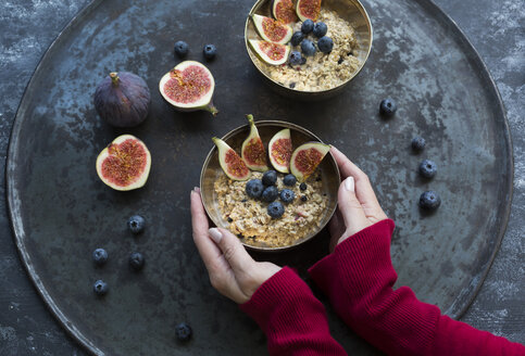 Woman's hands holding bowl of porridge with sliced figs, blueberries and dried berries - JUNF01389