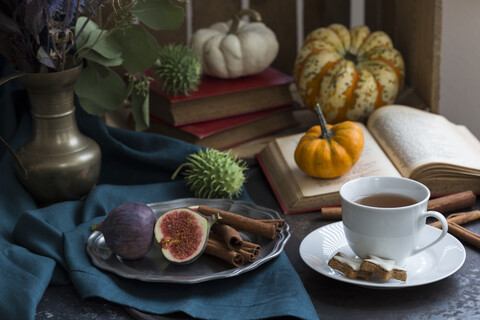 Herbstliches Stillleben mit Feigen, Zimtstangen, Büchern und einer Tasse Tee, lizenzfreies Stockfoto