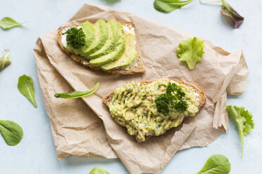 Slices of bread with sliced avocado and avocado cream on brown paper - JUNF01407