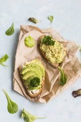 Slices of bread with sliced avocado and avocado cream on brown paper - JUNF01408