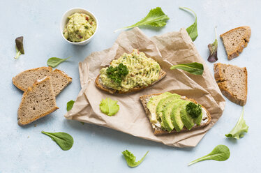 Slices of bread with sliced avocado and avocado cream on brown paper - JUNF01409