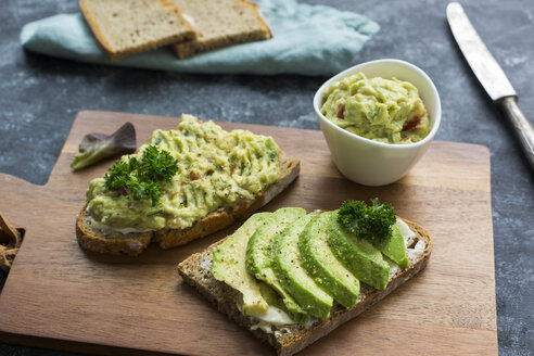 Slices of bread with sliced avocado and avocado cream on wooden board - JUNF01412