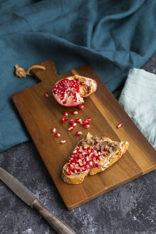 Brotscheibe mit Erdnussbutter, Granatapfelkernen und Schokoladenstückchen auf Holzbrett - JUNF01420