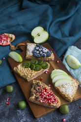 Bread slices with various toppings on wooden board - JUNF01423