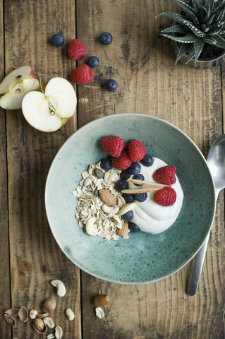 Breakfast bowl with granola, yogurt, nuts, apple, raspberry, blueberry on wood stock photo