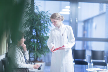 Radiologe, der ein digitales Tablet hält, im Gespräch mit einer reifen Frau im Wartebereich eines Krankenhauses - CUF44206