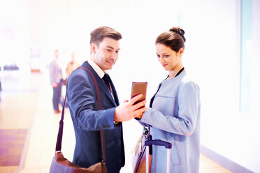 Junge Geschäftsfrau und Mann im Flughafen schauen auf ihr Smartphone - CUF44224