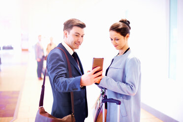 Young businesswoman and man in airport looking at smartphone - CUF44224