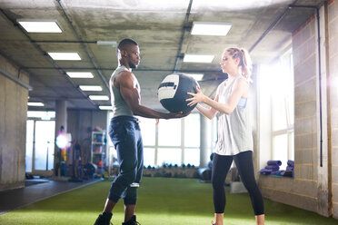 Trainer übergibt Medizinball an Kundin im Fitnessstudio - CUF44251