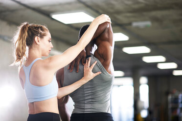 Trainerin hilft Mann bei Dehnungsübungen im Fitnessstudio - CUF44259