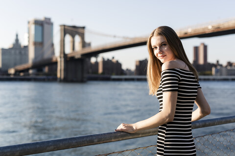 USA, New York, Brooklyn, Porträt einer Frau vor dem East River bei Sonnenuntergang, lizenzfreies Stockfoto