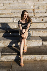 Porträt einer jungen Frau, die auf einer Treppe sitzt und den Sonnenuntergang genießt - GIOF04563