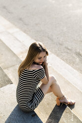 Young woman wearing striped dress relaxing on stairs enjoying sunset - GIOF04568